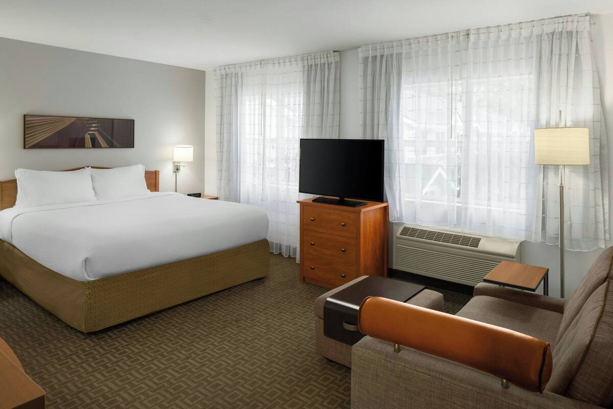 A hotel room with a large bed, a television, a desk, and a chair.
