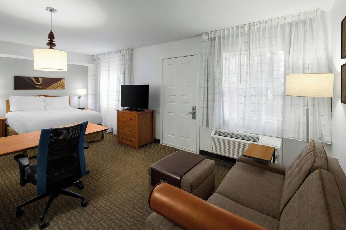 A hotel room with a bed, desk, office chair, sofa, television, and a window with curtains.