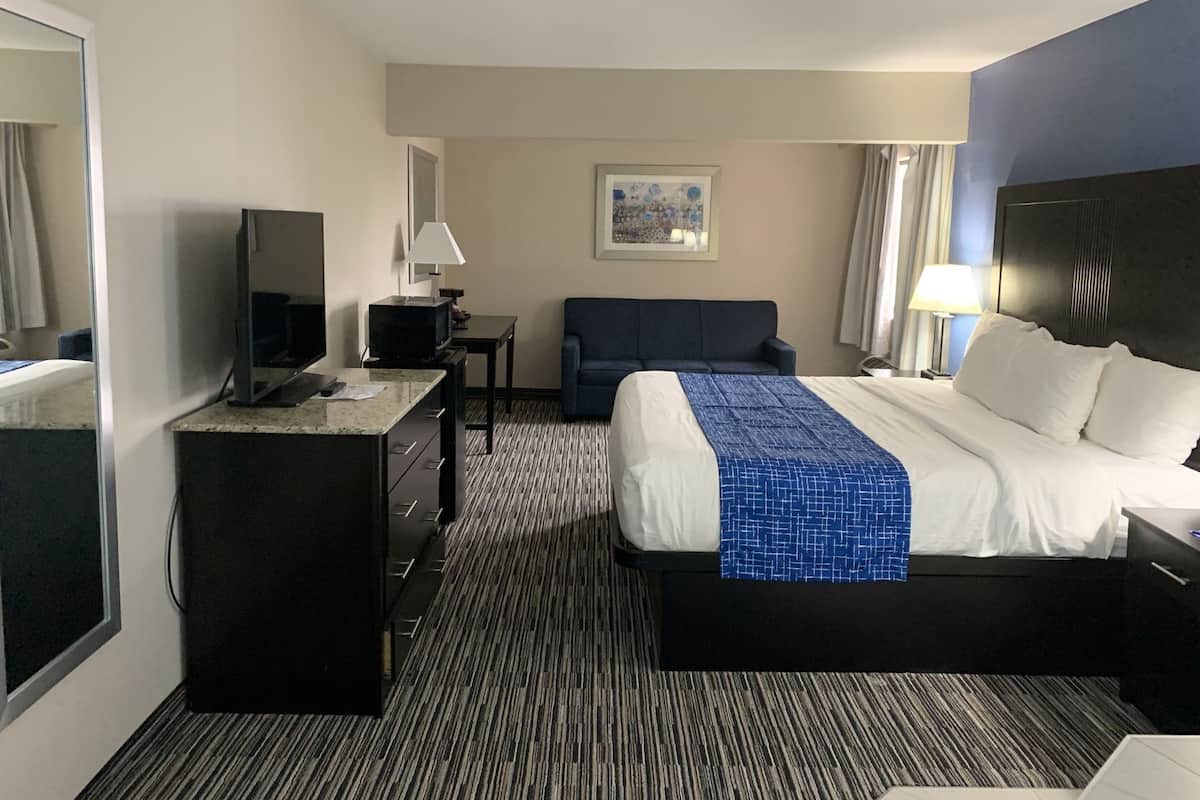 A hotel room with a bed, a desk, a TV, a sofa, and a painting on the wall.