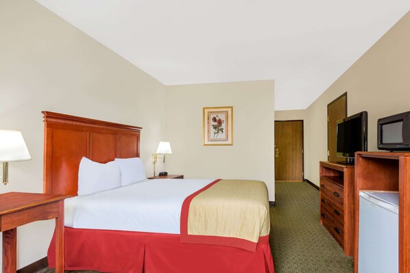 A hotel room with a bed, bedside tables, a television, a refrigerator, and a door leading to another room. - Baymont by Wyndham Enid (Enid)