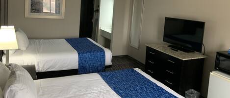 Una habitación de hotel con dos camas, un televisor, un aparador y un cuadro en la pared.