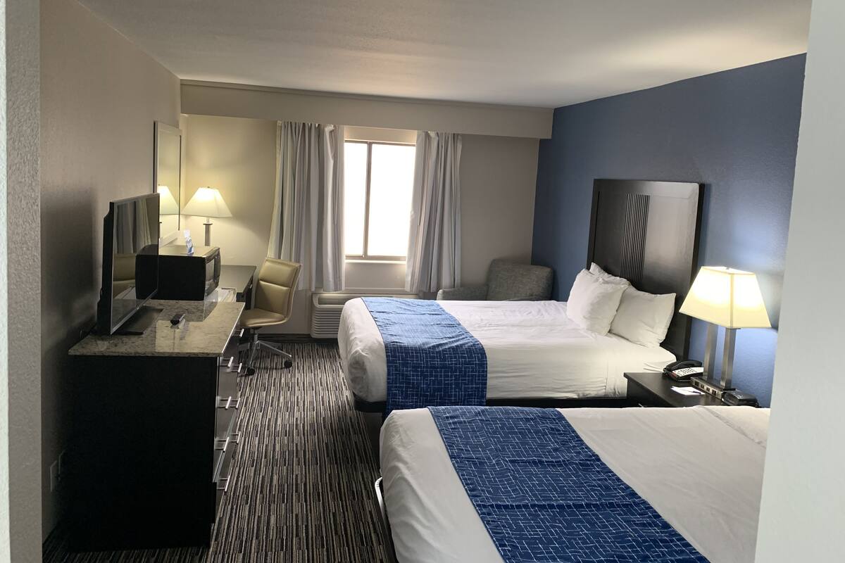 A hotel room with two beds, a desk, a chair, a TV, and a window with curtains.