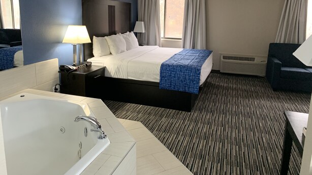 A hotel room with a large bed, a separate bathroom with a bathtub, a desk, and a chair. - Baymont by Wyndham Enid (Enid)
