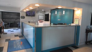 A reception desk with a blue and white color scheme, a television mounted on the wall, and a sign indicating the hotel's name and breakfast hours. - Baymont by Wyndham Enid (Enid)