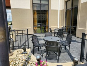 Une terrasse extérieure avec des tables et des chaises rondes, un chemin de pierre et une vue sur la rue à travers de grandes fenêtres.