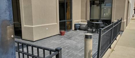 An outdoor patio area with a table and chairs, a potted plant, and a metal bollard.