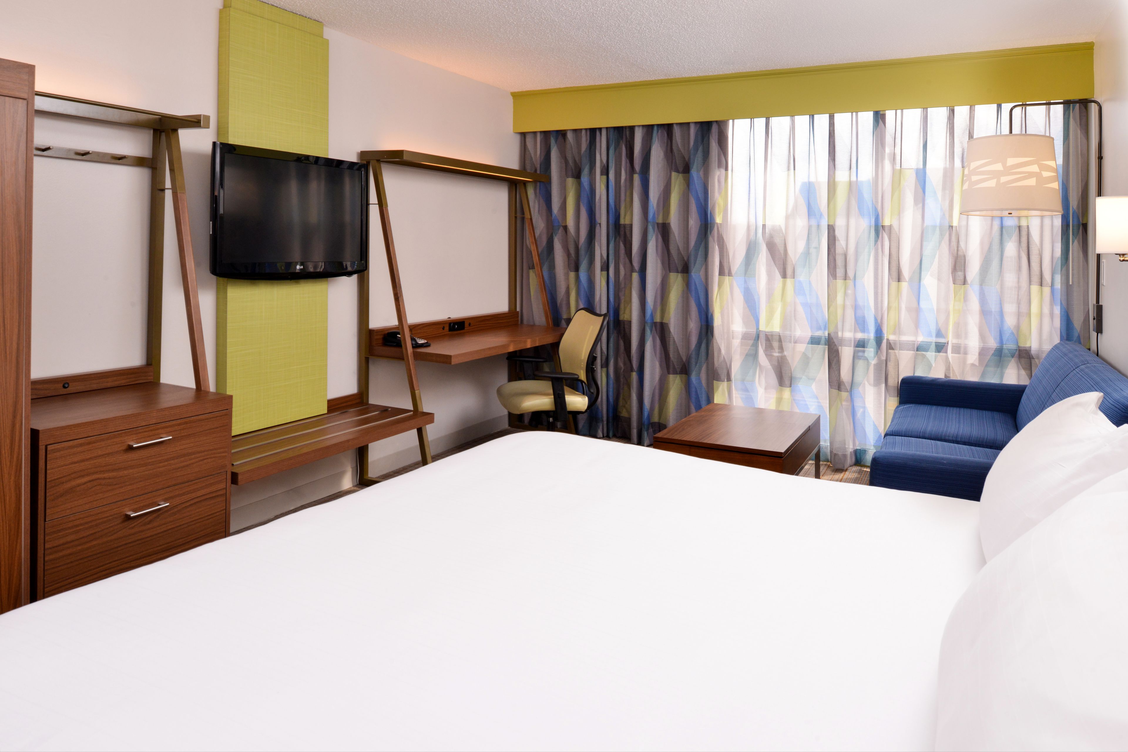 A hotel room with a bed, a desk, a chair, a TV, and a sofa.