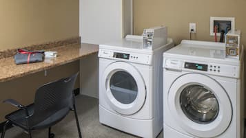 A laundry area with two front-loading washers, a small table with a bag and a box, and a chair.