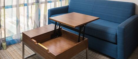 A room with a blue sofa, a wooden table with a metal frame, and a patterned curtain.