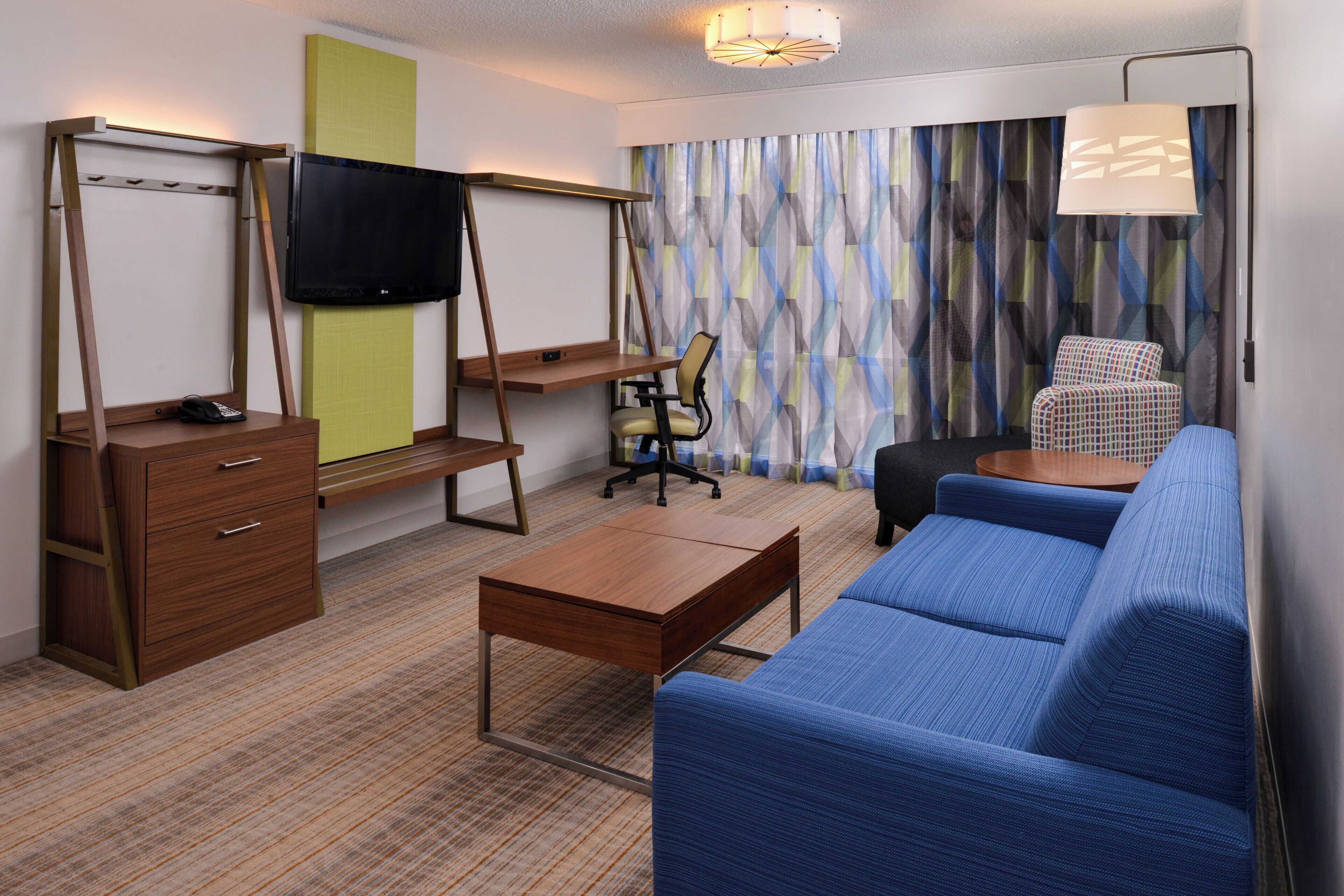 Ein Hotelzimmer mit einer Couch, einem Schreibtisch, einem Sessel, einem Fernseher und einem Bett.