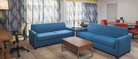A hotel room with two sofas, a coffee table, a desk with a chair, and a small table with a chair.