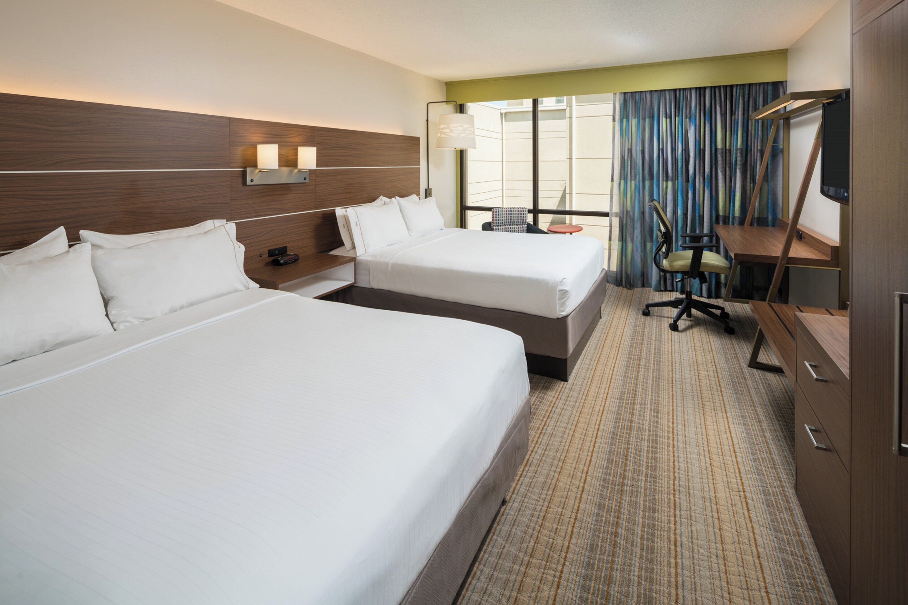 A hotel room with two beds, a desk, a chair, and a television.