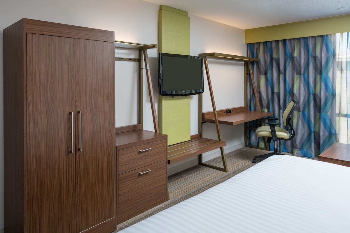 A hotel room with a bed, a desk with a chair, a TV on a stand, and a wardrobe.