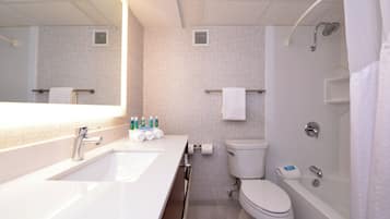 A modern bathroom with a large mirror, dual sinks, a toilet, and a bathtub.