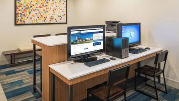 Un salón de conferencias con dos computadoras de escritorio, un monitor grande y una disposición de asientos.
