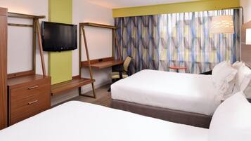 A hotel room with a bed, a desk with a chair, a television, and a window with curtains.