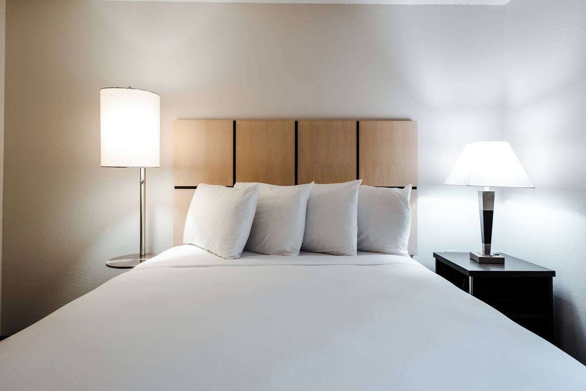 A neatly made bed with white linens and a wooden headboard. There are two bedside tables, each with a lamp.
