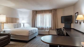 A hotel room with a bed, a desk, a chair, a TV, and a window with curtains.