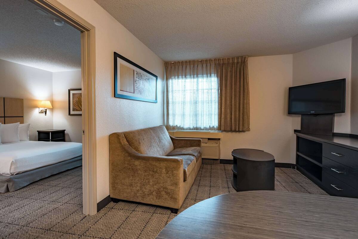 Ein Hotelzimmer mit Bett, einer Couch, einem Schreibtisch, einem Fernseher und einem Fenster mit Vorhängen.