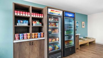 Un mostrador con productos de snacks, un refrigerador lleno de bebidas y una estantería con conservas.