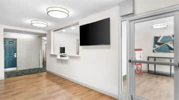 Un moderno vestíbulo de hotel con suelo de madera, un televisor de pantalla plana montado en la pared, un mostrador de recepción y una puerta de vidrio que da a otra habitación.