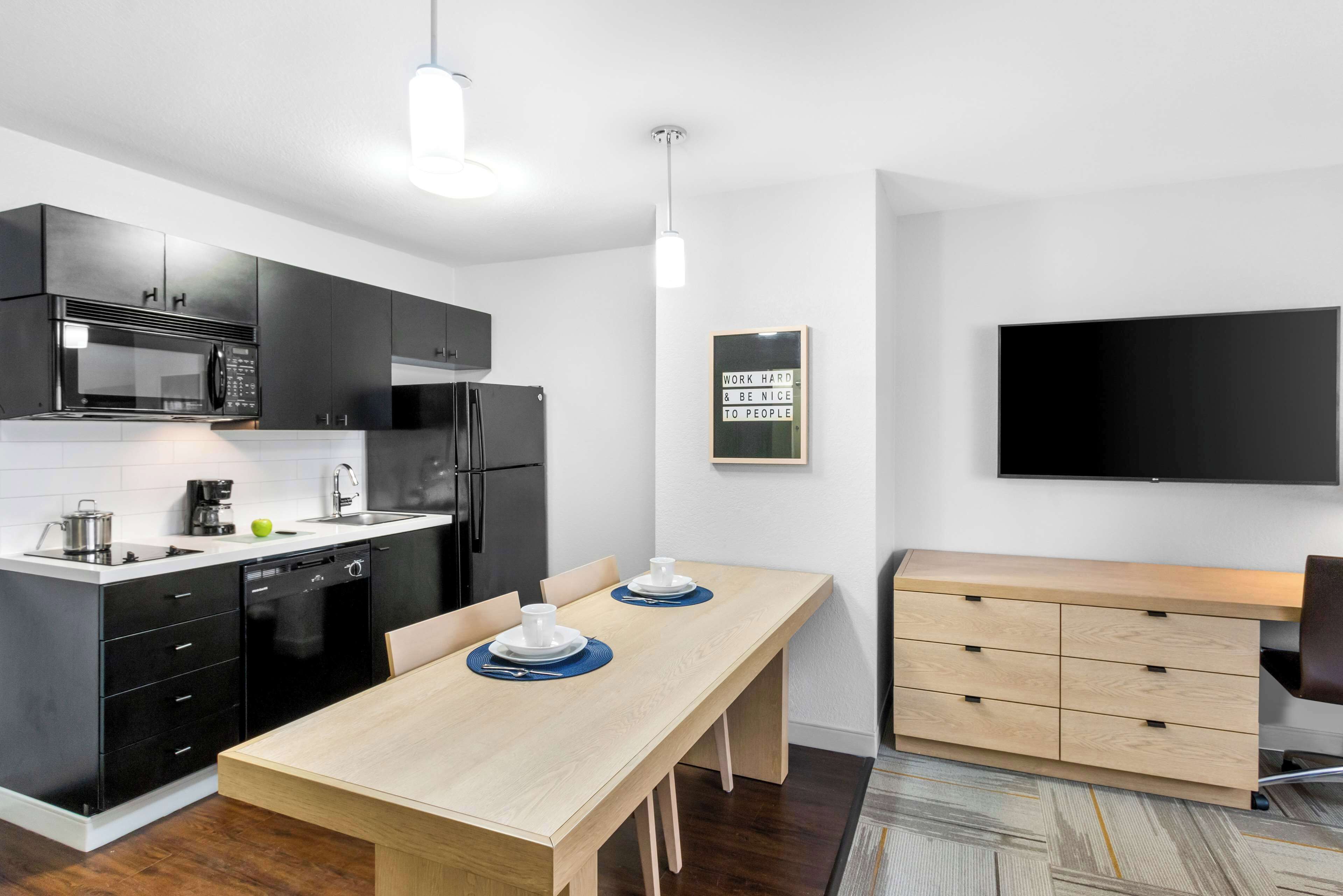 Una cocina moderna con armarios negros, una mesa de comedor de madera y un televisor de pantalla plana montado en la pared.