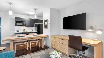 Et moderne køkken med spiseplads, et fladskærms-tv og en arbejdsplads med stol.