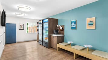 A modern reception area with a wooden bench, a coffee machine, and a refrigerator.