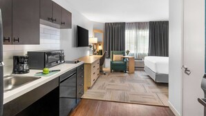 A compact hotel room with a kitchenette, a bed, a desk, and a chair. - Sonesta Simply Suites Austin South (Austin)