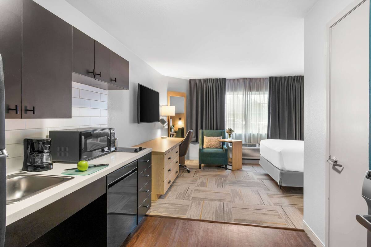 Una habitación de hotel pequeña con kitchenette, una cama, un escritorio y una silla.