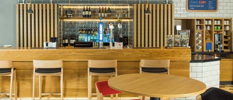 Een bar met een houten toonbank, barstoelen en een koffieapparaat.