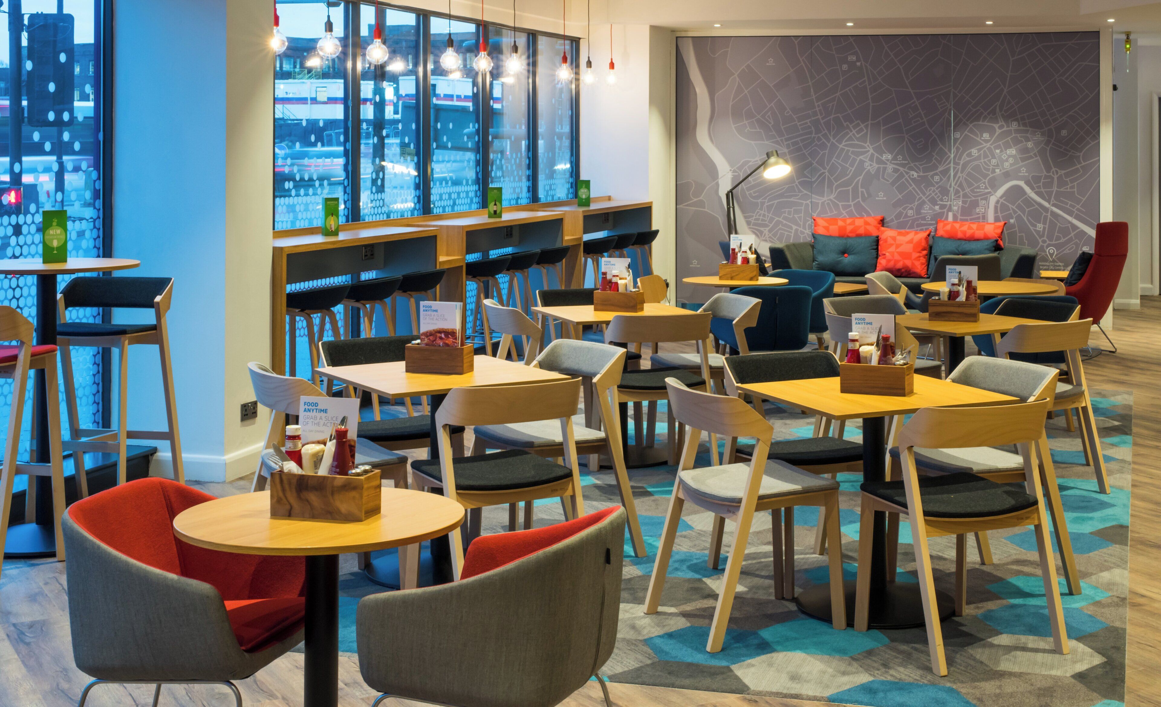 A modern restaurant with round tables and chairs, a large window with city views, and a map wall.