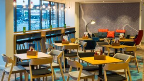 A modern restaurant with multiple seating areas, including tables and chairs, and a large window offering a view of the city. - Holiday Inn Express Bristol City Centre by IHG (Bristol)