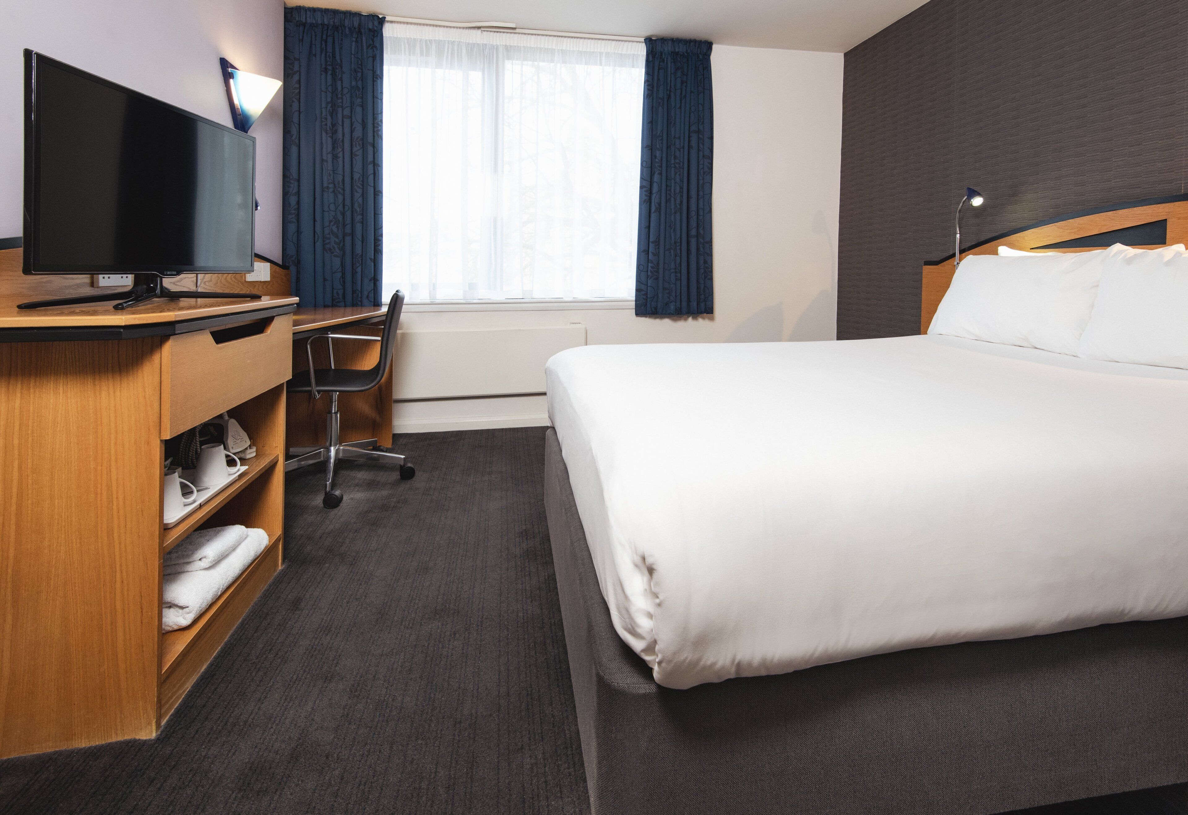 Habitació d'hotel amb un llit, una taula de treball amb un ordinador, una cadira i un televisor.