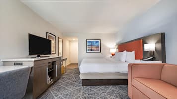 A hotel room with a bed, a TV, a desk, a sofa, and a painting on the wall.