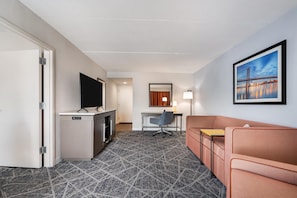 Quarto de hotel com televisão, escrivaninha, cadeira, sofá e um quadro na parede.