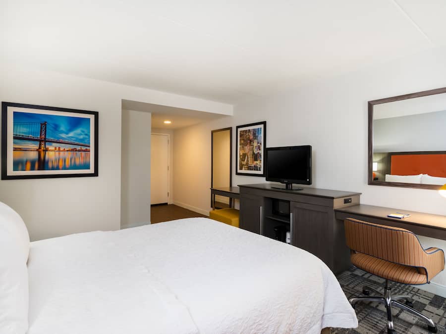 Habitación de hotel con cama, escritorio, silla, televisor y obras de arte en las paredes.
