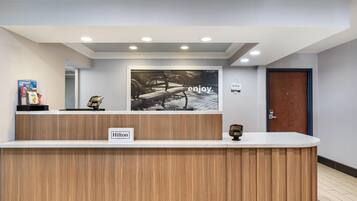 Una recepción de hotel con un cartel que dice 'Enjoy', un cartel de 'Hilton', un teléfono y una pequeña estatua.