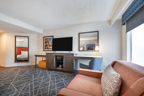A hotel room with a sofa, a TV, a desk, and a mirror.
