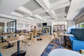 Un hall d’hôtel moderne offrant différents types de sièges, notamment des tables et des canapés, un tapis à motifs et une cheminée.