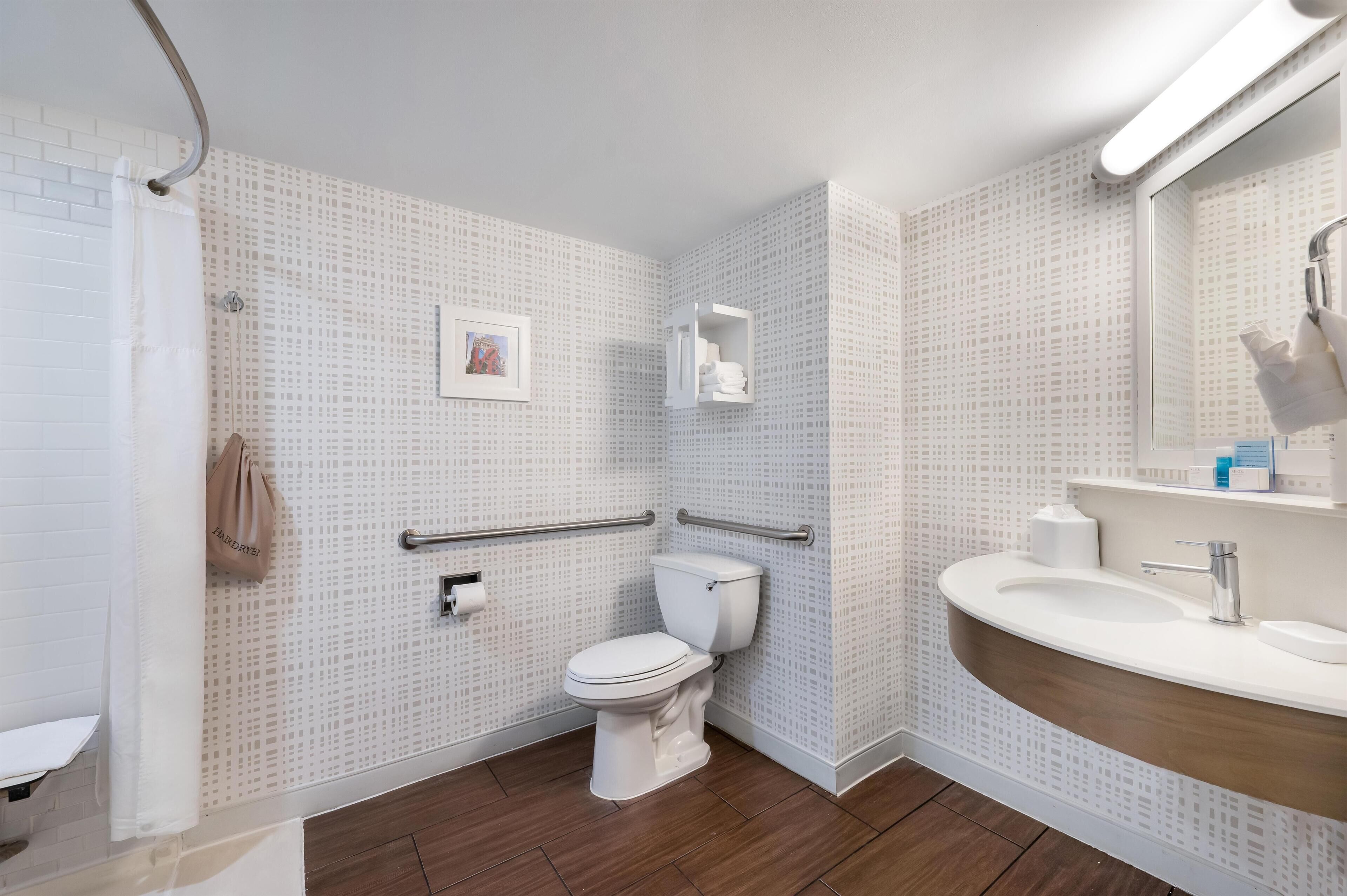 A bathroom with a white toilet, a shower area, a sink with a mirror, and a towel rack.