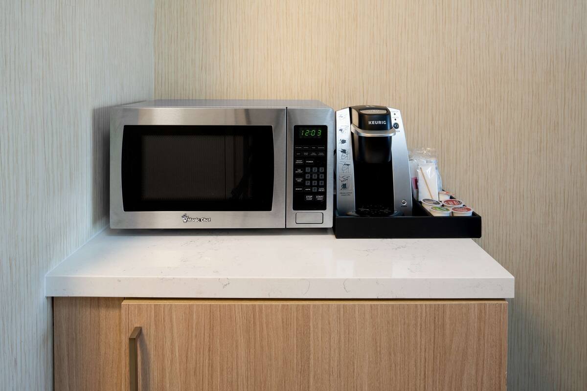 A microwave and coffee maker on a white countertop with a wooden cabinet below.