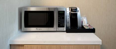 A microwave and coffee maker on a white countertop with a wooden cabinet below.