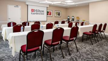 A conference room with tables and chairs, a projector screen displaying Hilton Garden Inn logo, and a door.