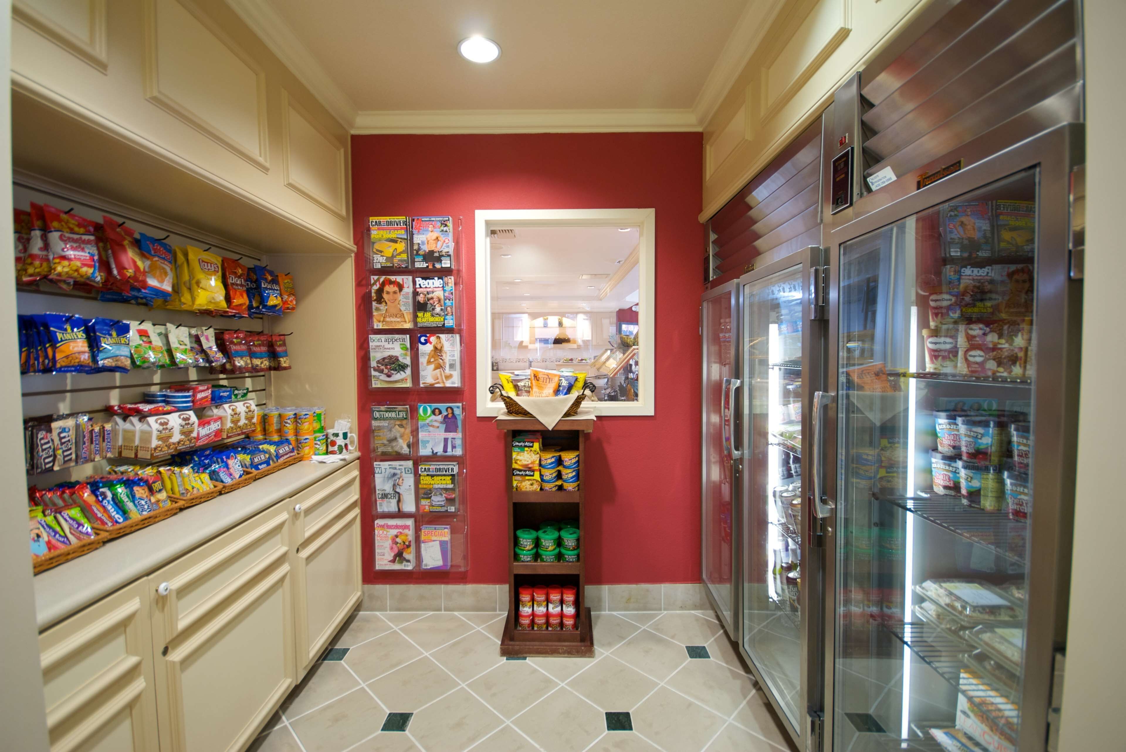 A kitchen with a red wall, a refrigerator, and shelves stocked with snacks and condiments.