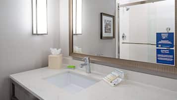 A modern bathroom with a large mirror, a sink, and a toilet. There is a framed picture on the wall and a sign about cleanliness.