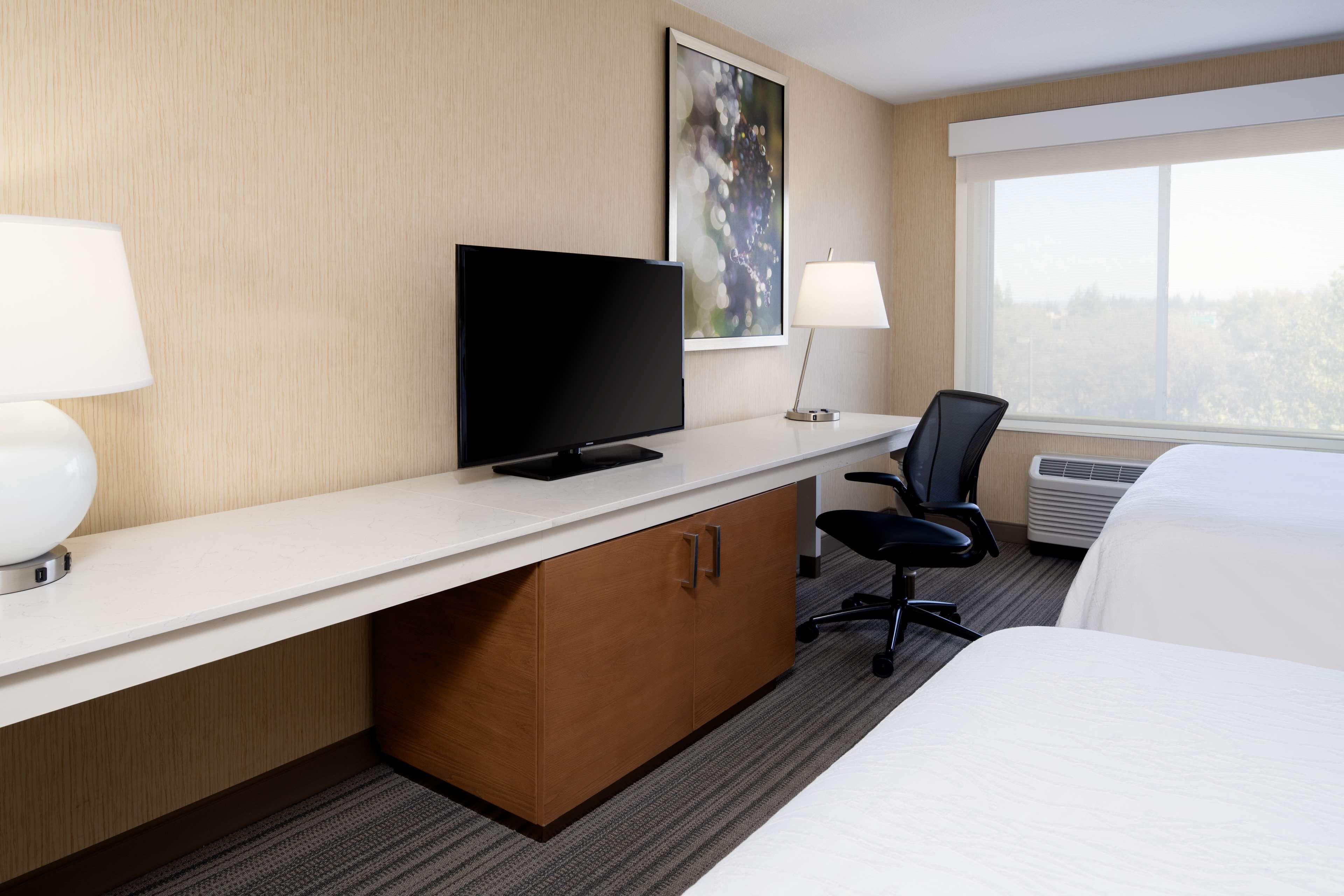 Una habitación de hotel con una cama, un escritorio con televisor, una silla y una ventana con vistas.