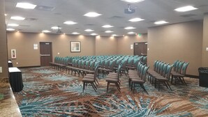 A conference room with rows of chairs, a patterned carpet, and a projector on the ceiling.