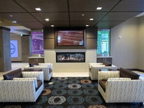 A lounge area with sofas, a fireplace, a flat-screen TV, and a patterned carpet. - Holiday Inn South Jordan - SLC South by IHG (South Jordan)