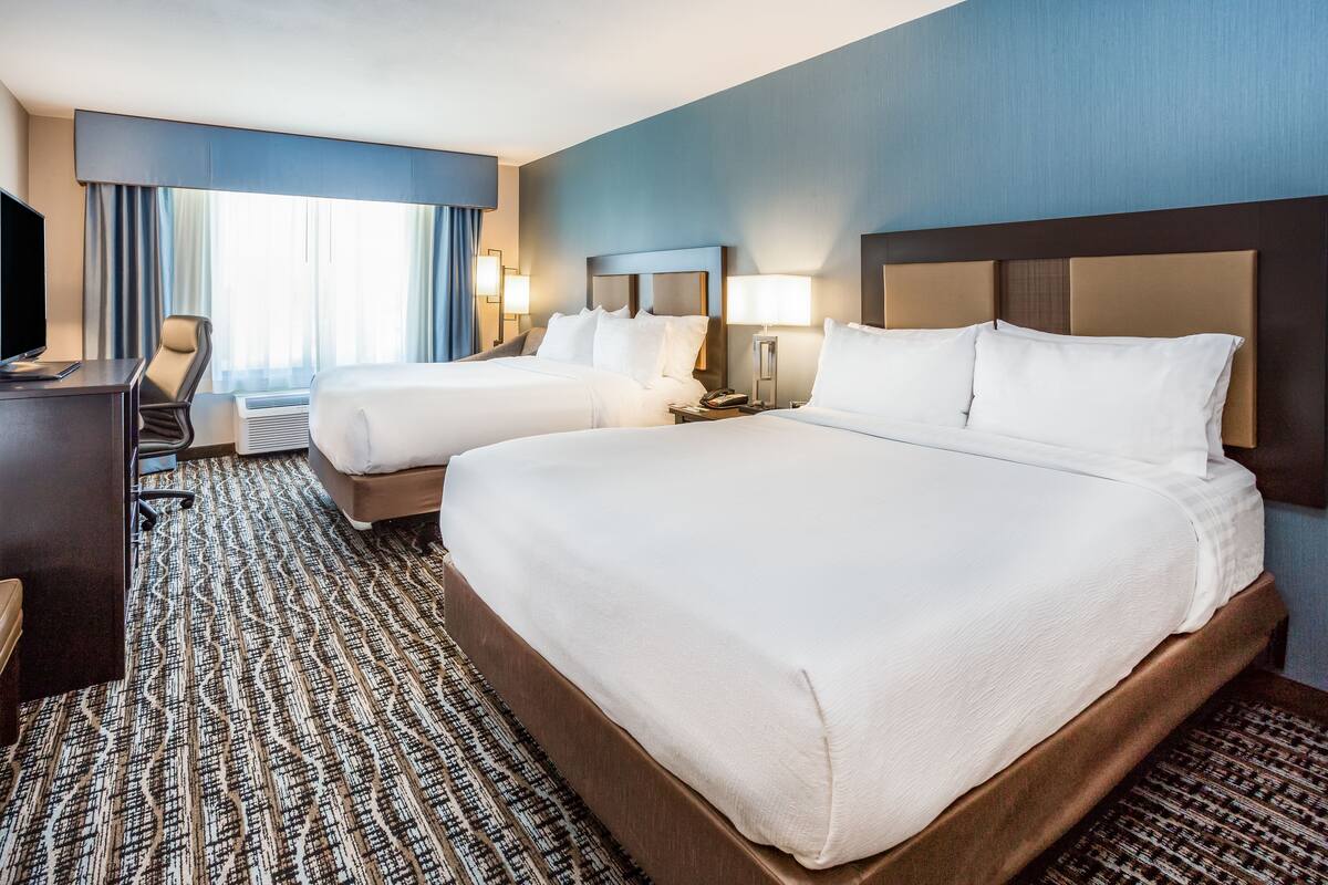 A hotel room with two beds, a desk, and a television.